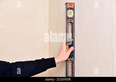 Die Hand des Arbeiters hält die Wasserwaage. Prüfen Sie die Neigung der Wand mit Gebäudeebene Stockfoto