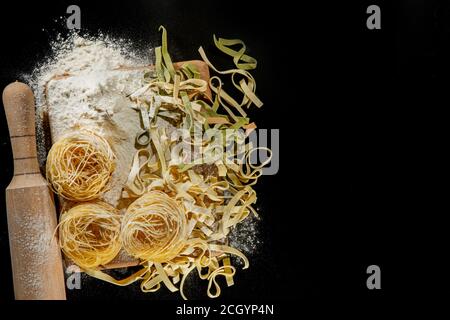 Frisch gekochte Pasta liegt auf einer dunklen, mit Mehl bestäubten Oberfläche. Italienische Pasta. Tagliatelle. Rohe Pasta. Italienische Pasta Rezept. Draufsicht, Kopierbereich Stockfoto