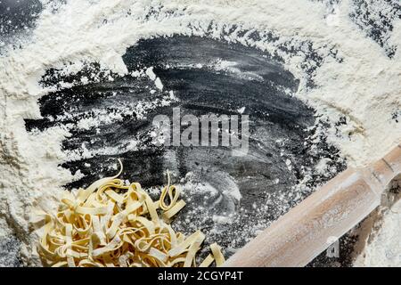 Frisch gekochte Pasta liegt auf einer dunklen, mit Mehl bestäubten Oberfläche. Italienische Pasta. Tagliatelle. Rohe Pasta. Italienische Pasta Rezept. Draufsicht, Kopierbereich Stockfoto