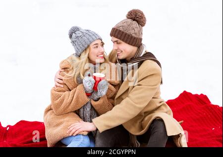 Romantisches Paar Sitzt Auf Plaid Bei Schnee Bedeckt Boden Und Kaffee Trinken Stockfoto