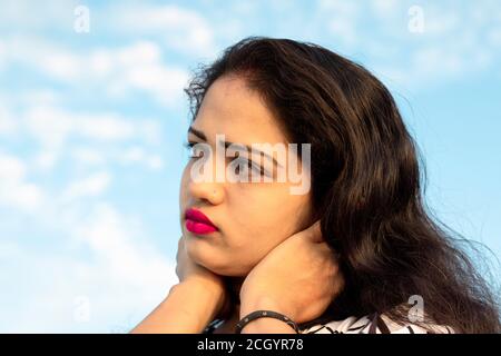 Nahaufnahme Foto von einem indischen Modell mit schönen Gesicht mit verschwommenem Hintergrund des Himmels mit weißen Wolken und Wegschauen Stockfoto