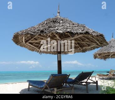 Strohschirm und zwei hölzerne Sonnenliegen an EINEM tropischen Strand, Sansibar Stockfoto