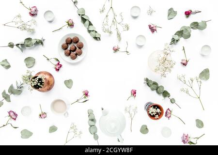 Arbeitsbereich mit Rosenknospen, Eukalyptus-Blätter, saftig, Tee, Tasse Kakao, Süßigkeiten auf weißem Hintergrund. Flach liegend, Ansicht von oben, Arbeitsplatz im Home Office Stockfoto