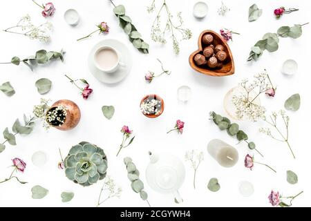 Arbeitsbereich mit Rosenknospen, Eukalyptus-Blätter, saftig, Tee, Tasse Kakao, Süßigkeiten auf weißem Hintergrund. Flach liegend, Ansicht von oben, Arbeitsplatz im Home Office Stockfoto