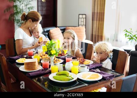 Gesunde Familie Frühstück zu Hause. Mutter und Kinder essen, tropische Obst, Toast, Brot, Käse und Wurst. Kinder trinken frisch gepressten Saft an sonnigen Stockfoto