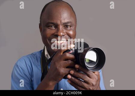 Afrikanischer Mann in blauem Hemd auf grauem Hintergrund vor ihm und Finger auf Kamera-Shutter lächelnd. Stockfoto