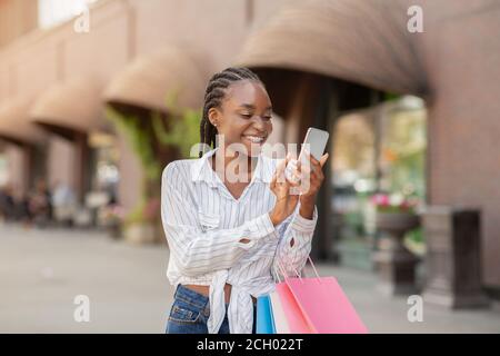 Porträt der Frau hält Pakete und Smartphone, schockiert von Online-Mode-Shop Stockfoto