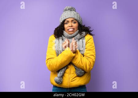 Unglücklich African Girl Einfrieren Tragen Von Winterkleidung Über Lila Hintergrund Stockfoto