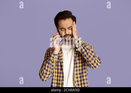Junger Inder mit Kopfschmerzen oder Depressionen auf dem Smartphone sprechen Über fliedem Hintergrund Stockfoto