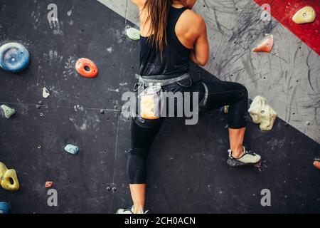 Attraktive sportliche Frau, die Bemühungen für einen großen Schritt auf eine künstliche bunte Wand mit Griffe und Haken. Stockfoto