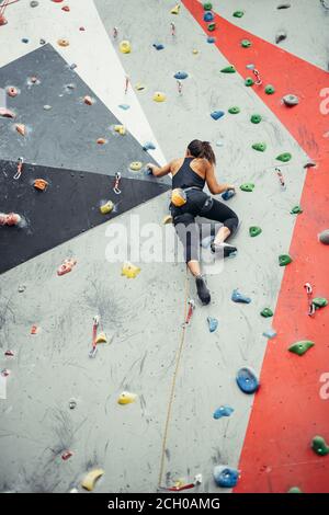 Attraktive sportliche Frau, die Bemühungen für einen großen Schritt auf eine künstliche bunte Wand mit Griffe und Haken. Stockfoto