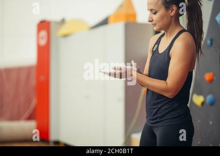 Junge Frau im dunkelgrauen Outfit Hände reiben mit Kreide bereitet sich auf das Training in der Kletterhalle vor Stockfoto