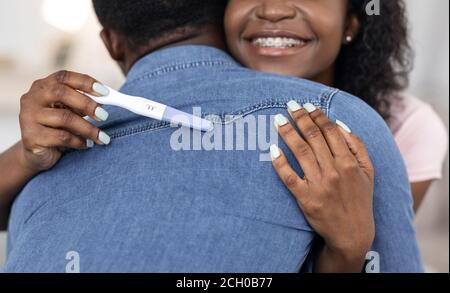 Von afrikanischer Frau mit Schwangerschaftstest umarmt Ehemann geschnitten Stockfoto