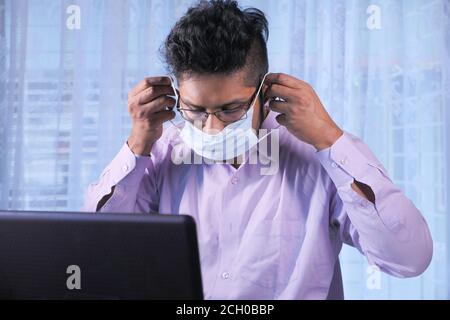 Junger Geschäftsmann trägt Schutzmaske und arbeitet am Laptop Stockfoto