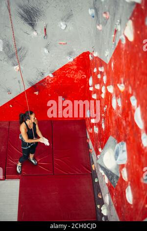 Hohe Betrachtungswinkel der sportlichen braunhaarige Frau Ausübung klettern auf bunte Rote künstliche Felsen in der Kletterhalle. Stockfoto
