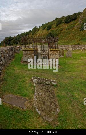 Ein gefallener und halb vergrabener Grabstein vor einer Grabbeigabe auf dem Friedhof von Nether kirk am Fuße der Klippen von St. Cyrus. Stockfoto