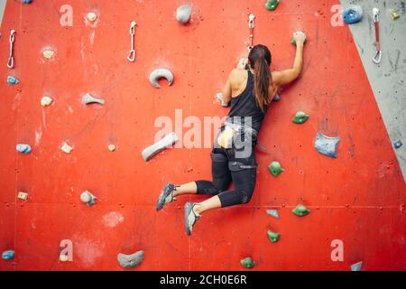 Attraktive sportliche Frau, die Bemühungen für einen großen Schritt auf eine künstliche bunte Wand mit Griffe und Haken. Stockfoto