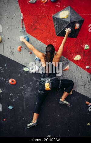 Attraktive sportliche Frau, die Bemühungen für einen großen Schritt auf eine künstliche bunte Wand mit Griffe und Haken. Stockfoto