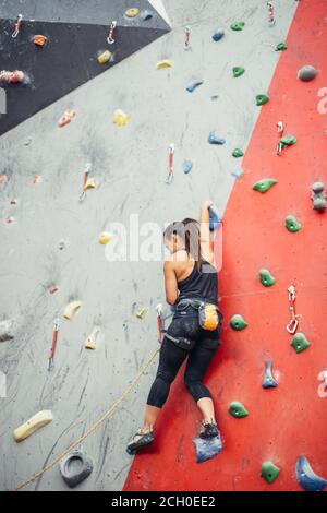 Attraktive sportliche Frau, die Bemühungen für einen großen Schritt auf eine künstliche bunte Wand mit Griffe und Haken. Stockfoto