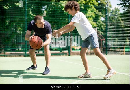 Fröhlicher Mann, der Junge lehrt, wie man Basketball spielt Stockfoto