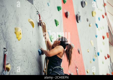 Attraktive sportliche Frau, die Bemühungen für einen großen Schritt auf eine künstliche bunte Wand mit Griffe und Haken. Stockfoto