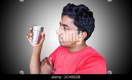 Ein Mann sitzt auf einem Stuhl und trinkt Tee zu Hause. Indischer junger Mann mit Tee oder Kaffeetasse Stockfoto