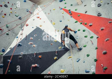 Attraktive sportliche Frau, die Bemühungen für einen großen Schritt auf eine künstliche bunte Wand mit Griffe und Haken. Stockfoto