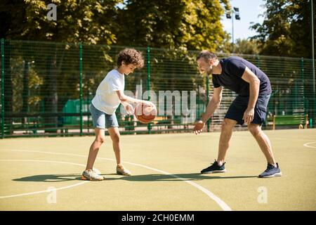 Sportlicher Mann, der Junge lehrt, wie man Basketball spielt Stockfoto