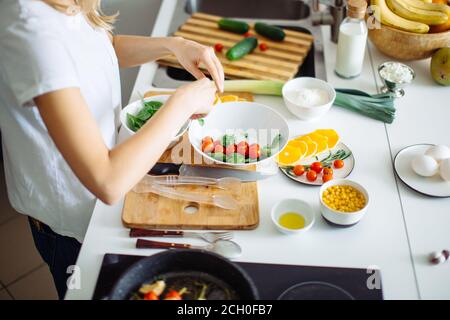 Beschnittene Ansicht der Frau, die gesunden Salat aus frischem Gemüse, Reißen Spinat in den Teller mit Tomatenkirsche und Spinat. Eine Pfanne mit Roa Stockfoto