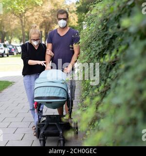 Besorgte junge Eltern, die mit einem Kinderwagen auf einer leeren Straße spazieren gehen und medizinische Masken tragen, um sie vor dem Corona-Virus zu schützen. Soziale Distanzierung Leben während Stockfoto