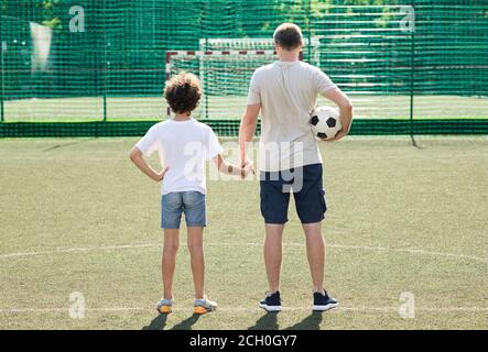 Papa posiert mit kleinen Jungen auf dem Fußballplatz, Rückansicht Stockfoto