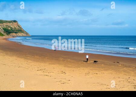 Ein paar Schritte am Cattersty Sands Beach in Skinningrove Cleveland entlang Großbritannien und ein Mann geht mit seinem Hund Stockfoto