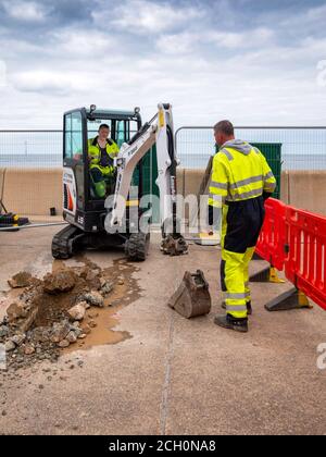 Arbeiter mit Bob Cat Bagger Bagger Aushub einer Kabelgraben Anschluss an einen Schaltschrank am Meer Wand in Redcar Stockfoto