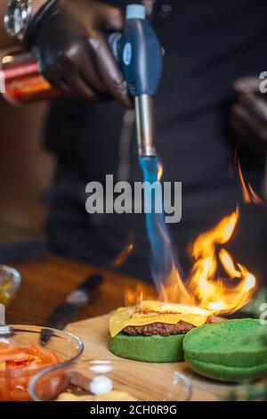 Koch nimmt an BurgerChef Competition brennenden Käse auf Burger-Brötchen mit kulinarischen Brenner für Burger. Gastronomie und Street Food Trend. Stockfoto