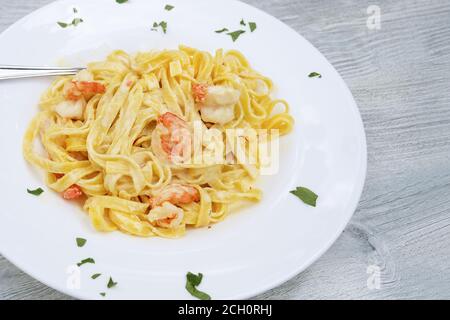 Tagliatelle Pasta mit Garnelen und Safransauce in einem weißen Teller auf einem grauen Holztisch, Kopierraum, ausgewählter Fokus, enge Schärfentiefe Stockfoto