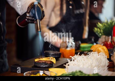 Koch nimmt an BurgerChef Competition brennenden Käse auf Burger-Brötchen mit kulinarischen Brenner für Burger. Gastronomie und Street Food Trend. Stockfoto