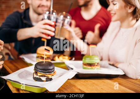 Freizeit, Feier, Getränke und Urlaub Konzept - glückliche Menschen und Freunde klirren Gläser des Getränks an der Burger-Bar. Verschiedene Burger auf w serviert Stockfoto