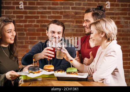 Freizeit, Feier, Getränke und Urlaub Konzept - glückliche Menschen und Freunde klirren Gläser des Getränks an der Burger-Bar. Verschiedene Burger auf w serviert Stockfoto