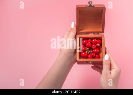 Frau öffnet eine Geschenkbox mit Schmuck. In einer Box in den Händen von Frauen auf einem rosa Hintergrund. Present Konzept. Stockfoto