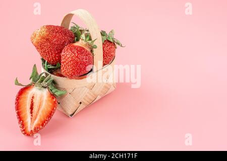 Rote Erdbeeren in kleinem Holzkorb oder Weide. Gesunde frische Beeren auf rosa Tisch mit Kopierer Platz. Sommer gesunde Ernährung. Stockfoto