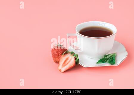 Tasse Tee auf einer weißen Untertasse mit Minzblättern und reifen Erdbeeren. Sommertee. Rosa Hintergrund. Copyspace. Stockfoto
