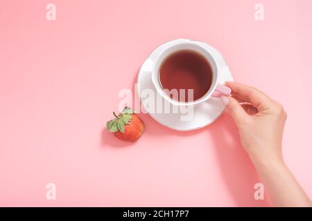 Frauenhand mit einer Tasse Tee und einer Erdbeere auf einem rosa Hintergrund. Draufsicht. Copyspace Stockfoto