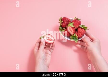 Nahaufnahme frisch geschälte Erdbeere in weißer Schale auf rosa Hintergrund. Eine Frauenhand nimmt Erdbeeren aus einer Schale Sommer gesundes Essen Konzept. Stockfoto