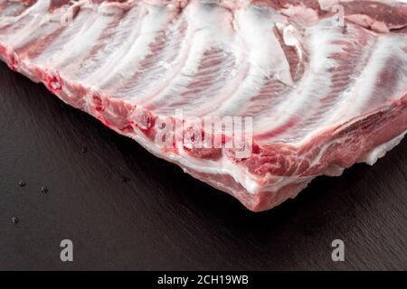 Whole raw pork ribs isolated on dark, black, stone board. spare ribs or belly. close-up. Raw meat, farm and cooking concept. Stock Photo