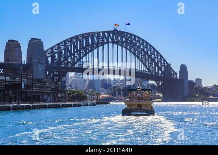 Sydney Harbour, Sydney, Australien. Eine Passagierfähre auf dem glitzernden Wasser, die in Richtung der ikonischen Harbour Bridge fährt Stockfoto