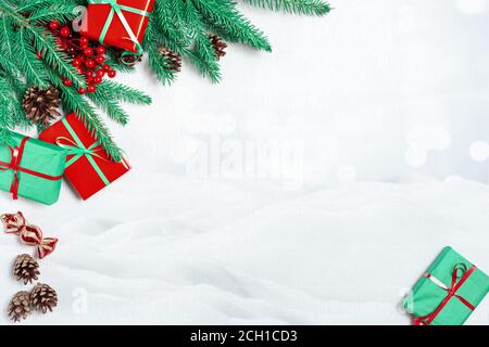 Weihnachten oder Winter Komposition. Weihnachtsrahmen aus Tannenzweigen, festliche Dekorationen, Geschenkschachteln, roten Stechbeeren und Tannenzapfen auf weißem Tabl Stockfoto