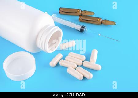 Pillen, Spritze, Ampullen für Injektionen auf einem blauen medizinischen Hintergrund. Nahaufnahme, Draufsicht. Medizinische Spritze mit Medikamentenpille und Fläschchen. Selektiver Fokus Stockfoto