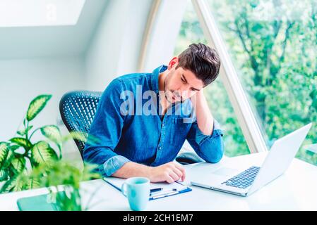 Aufnahme eines Geschäftsmannes mit Händen am Hals, der hinter seinem Laptop sitzt und unter starken Kopfschmerzen leidet. Stockfoto