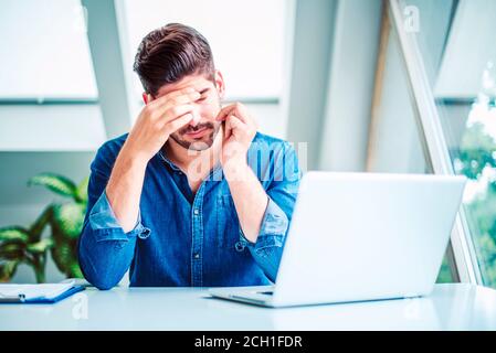 Aufnahme eines Geschäftsmannes mit der Hand auf der Stirn, die hinter seinem Laptop sitzt und unter starken Kopfschmerzen im Büro leidet. Stockfoto