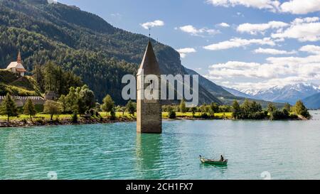 Fischer in seinem Boot in der Nähe des untergetauchten Glockenturms in Reschensee, Curon, Südtirol, Italien Stockfoto